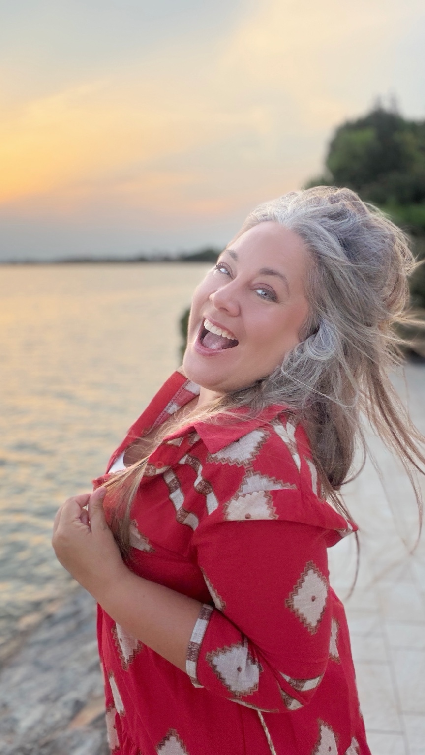 Karin lacht im roten Outfit am Wasser
