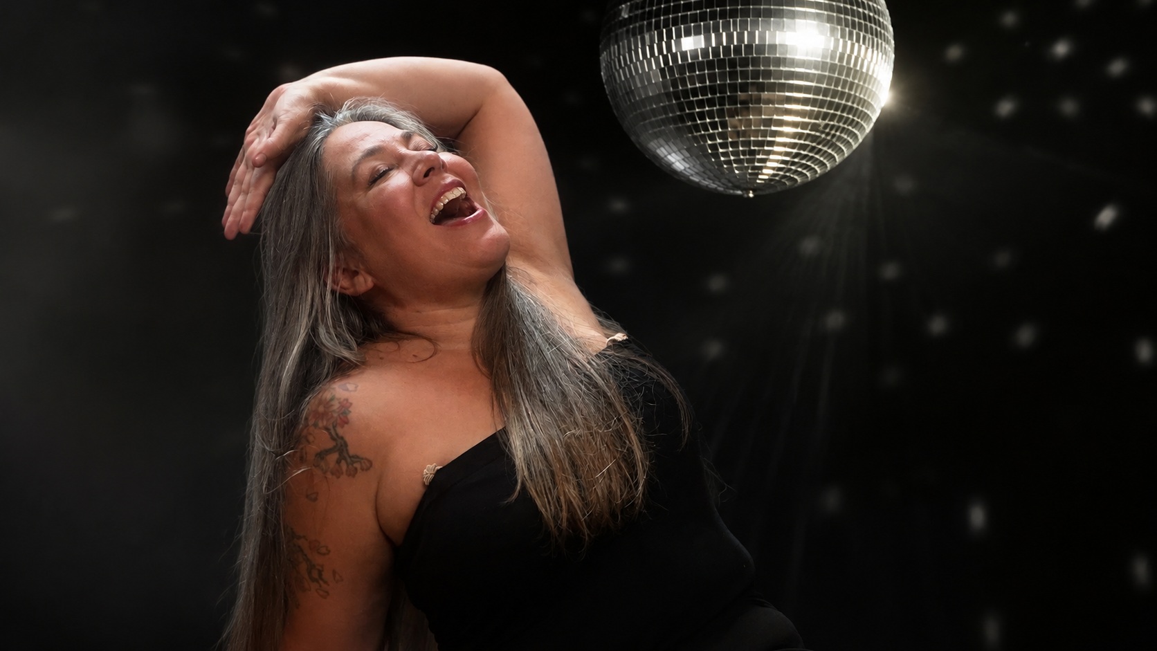 Karin im schwarzen Outfit vor dunkler Disco-Kulisse mit silberner Discokugel