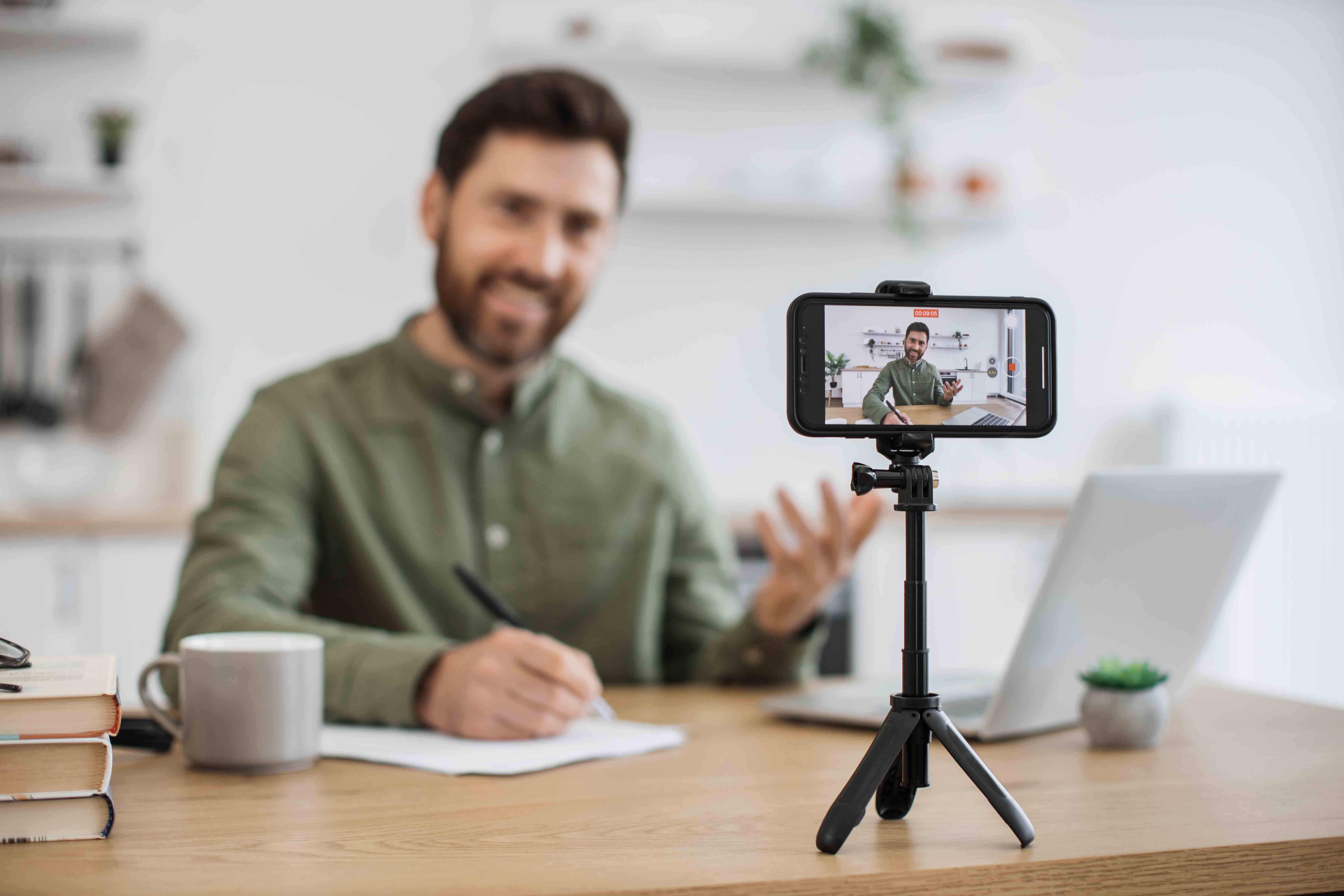 bearded-man-with-laptop-recording-video-on-smartph-2024-12-13-04-56-19-utc.jpg