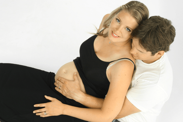Schwangere Frau mit Partner, der den Bauch umarmt