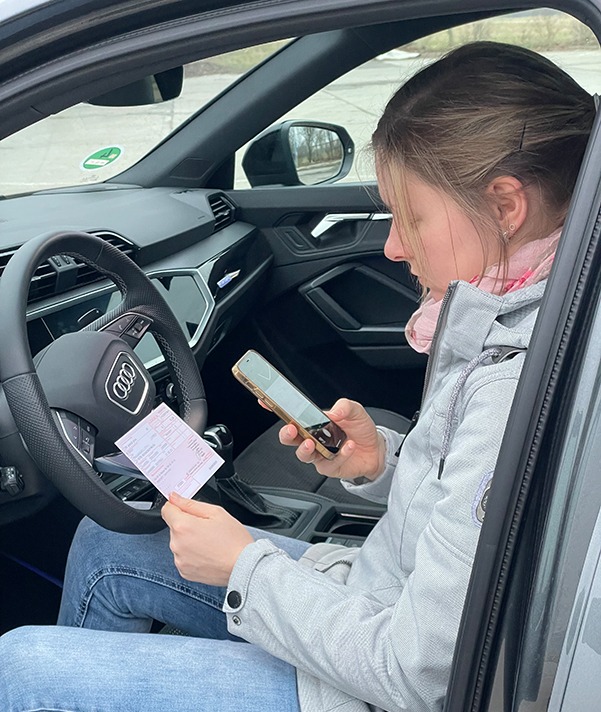 Frau sitzt im Auto und scannt ein Rezept mit dem Handy