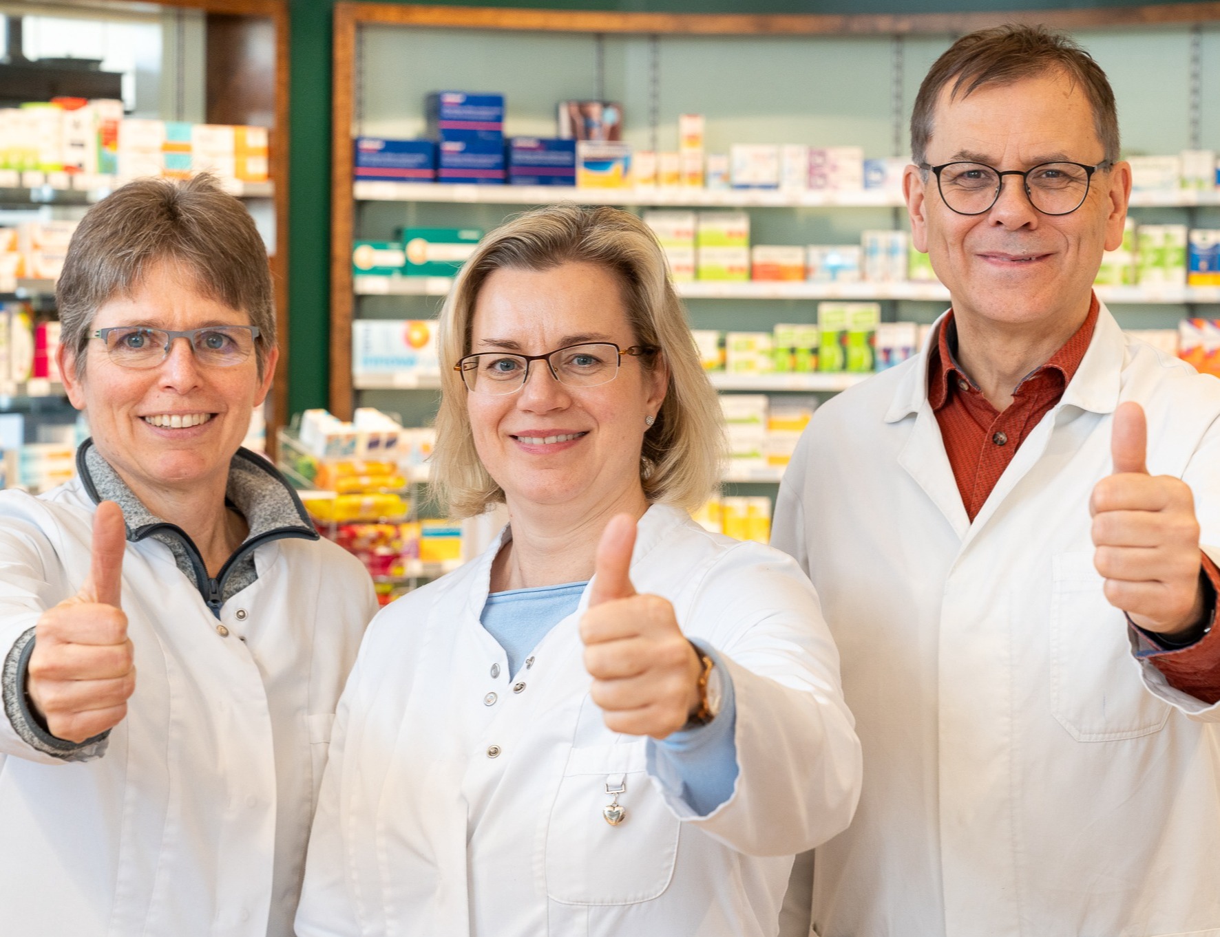 Drei lächelnde Mitarbeiter der Apotheke zeigen den Daumen nach oben