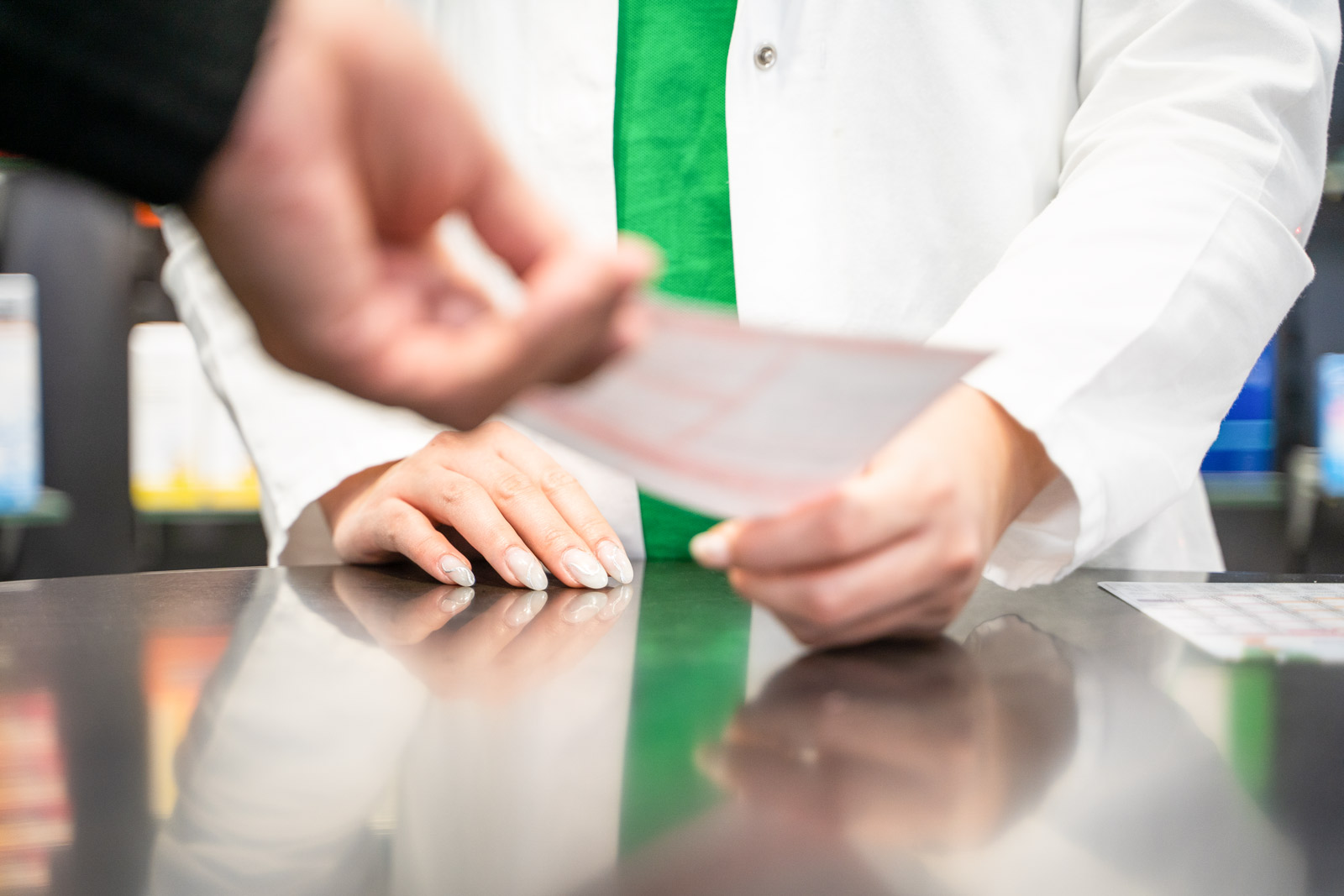 Ein Rezept wird über die Theke in die Hände einer Apothekerin übergeben
