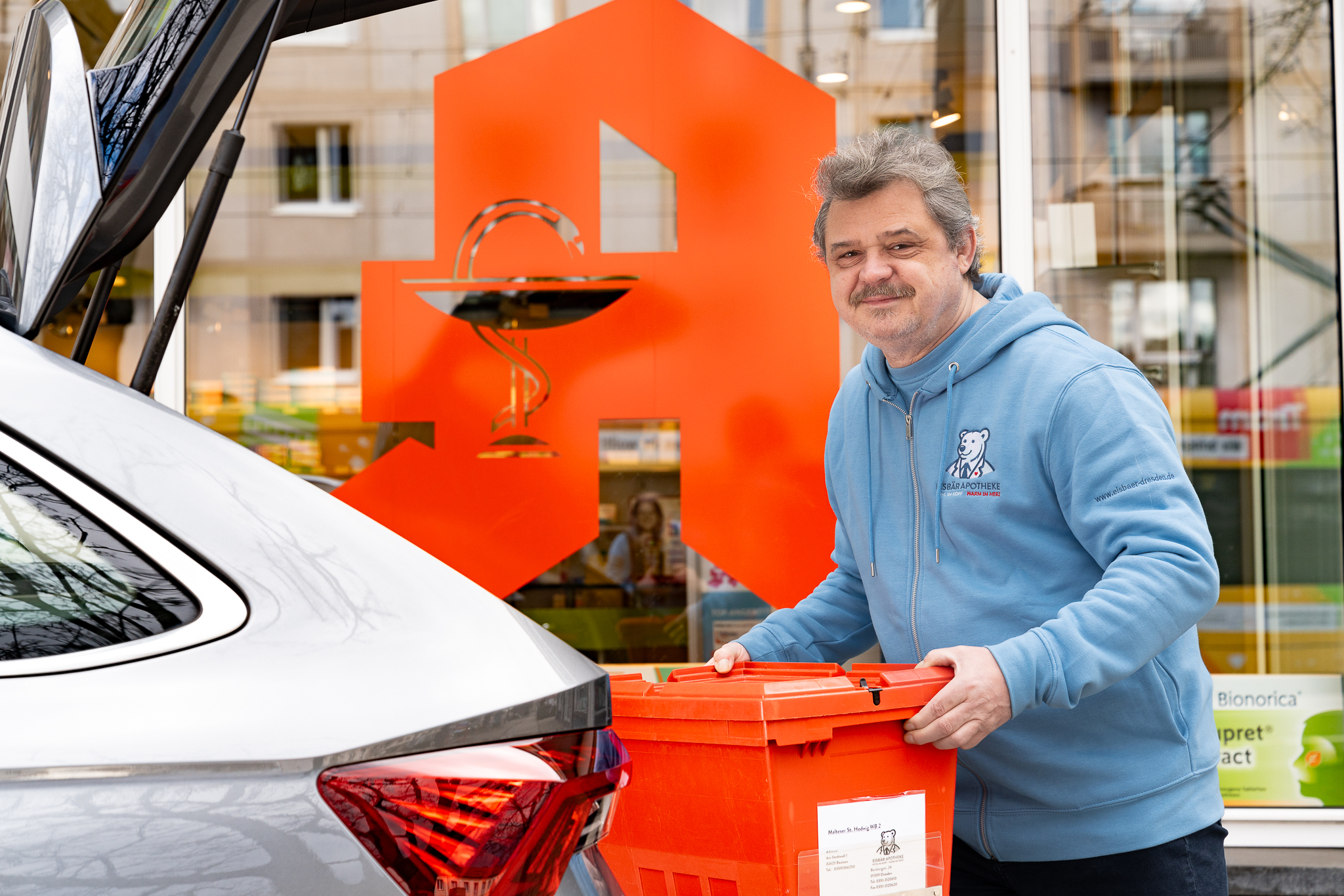 Mitarbeiter läd Medikamentenkiste in den Kofferraum des Lieferfahrzeugs