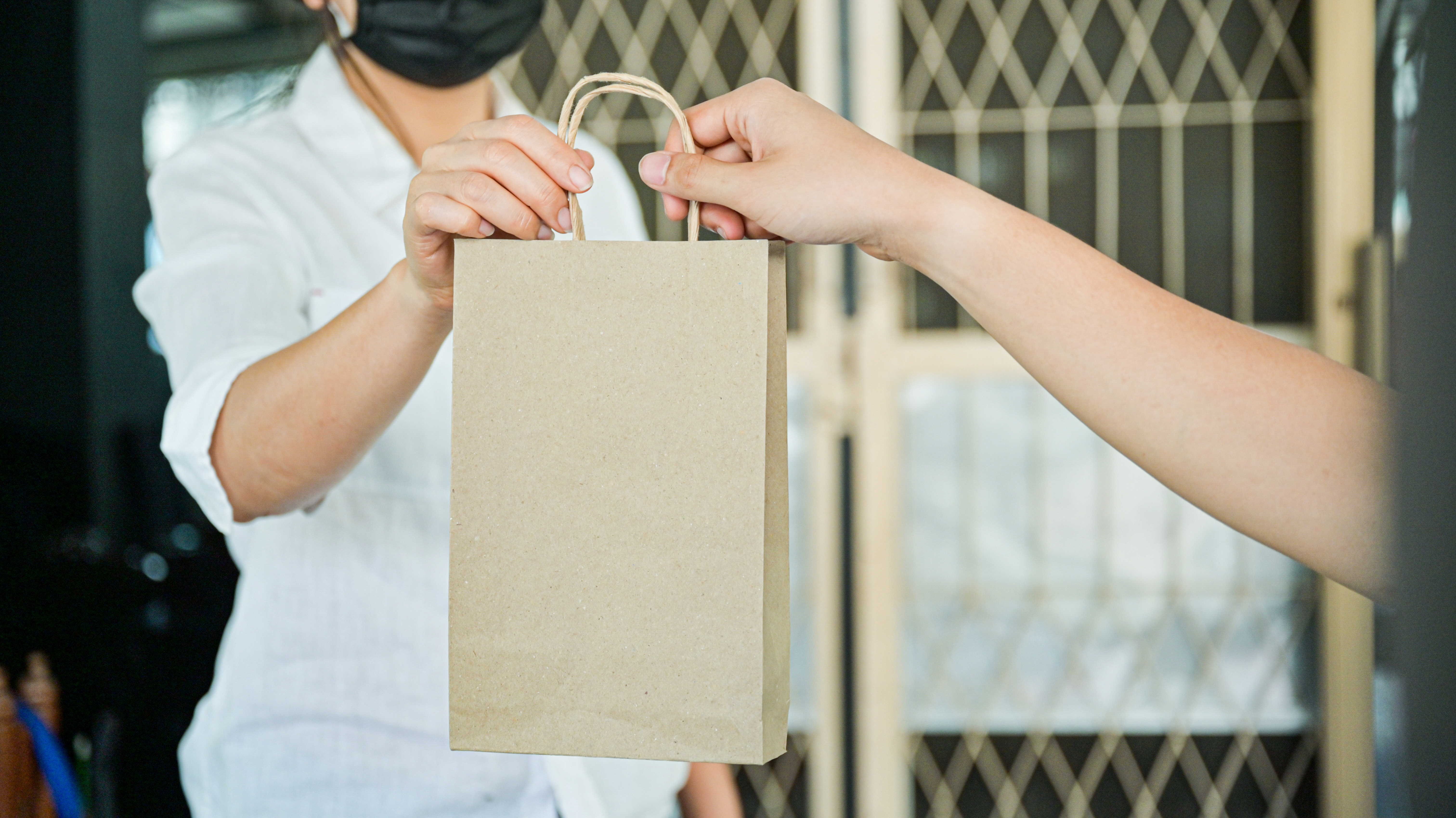 Eine Hand übergibt einer Frau eine Tüte mit Medikamenten