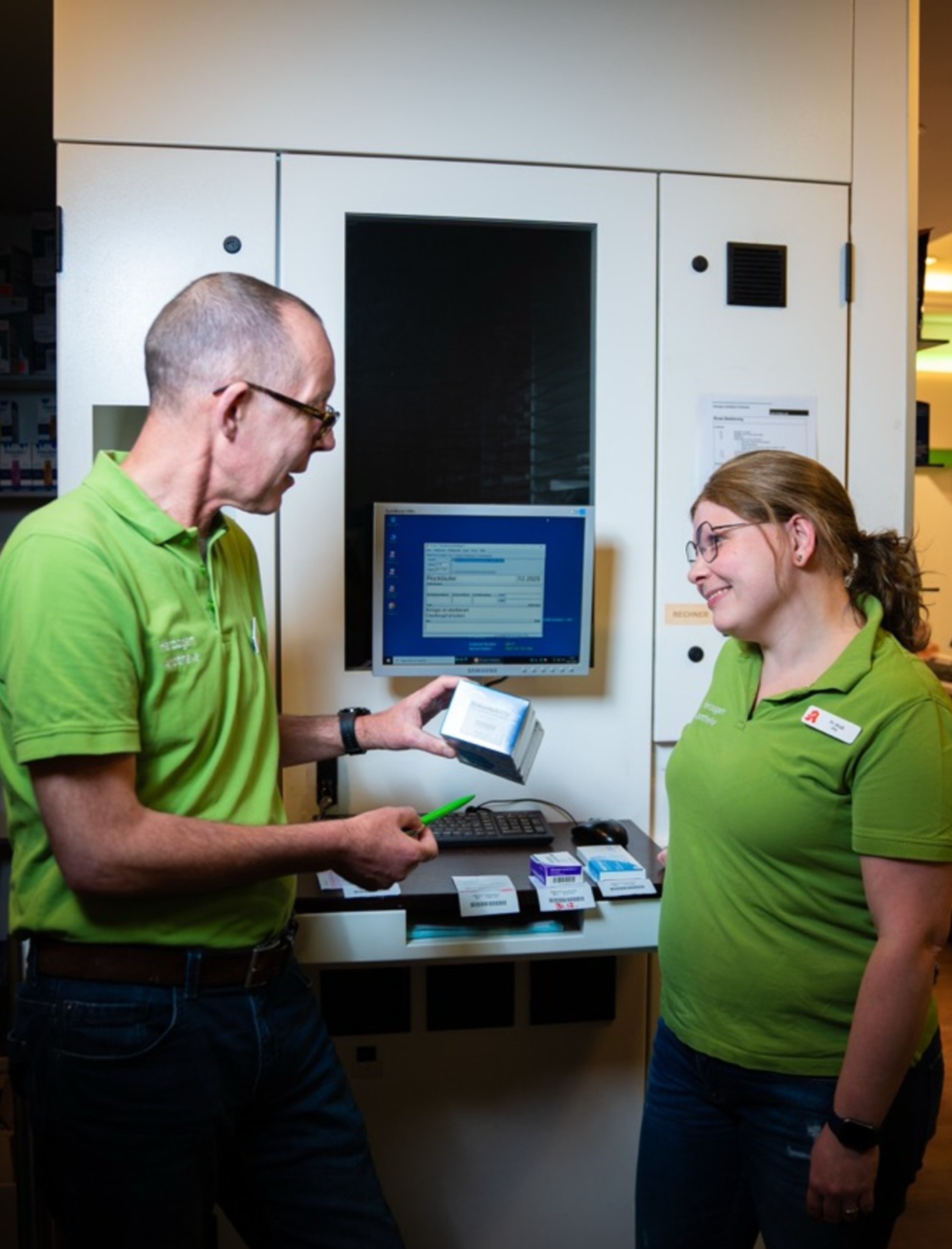 Vorschau Fotoshooting - Zwei Mitarbeiter der Apotheke unterhalten sich, einer hält ein Medikament