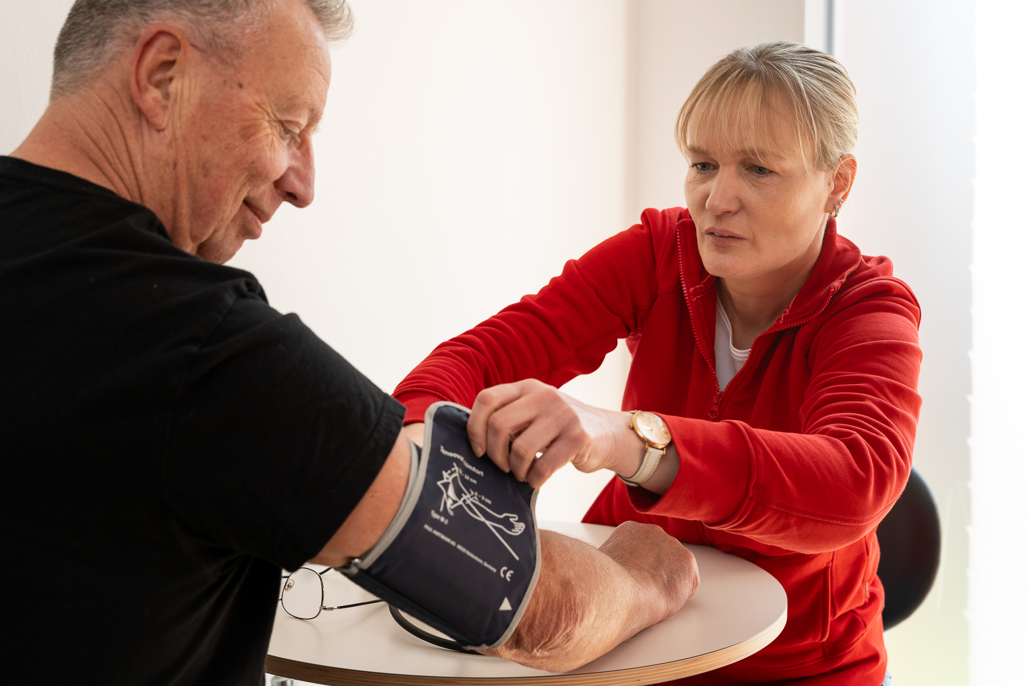 Mitarbeiterin misst den Blutdruck eines Kunden