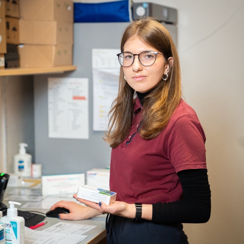 Mitarbeiterin am Computer hält ein Medikament in der Hand