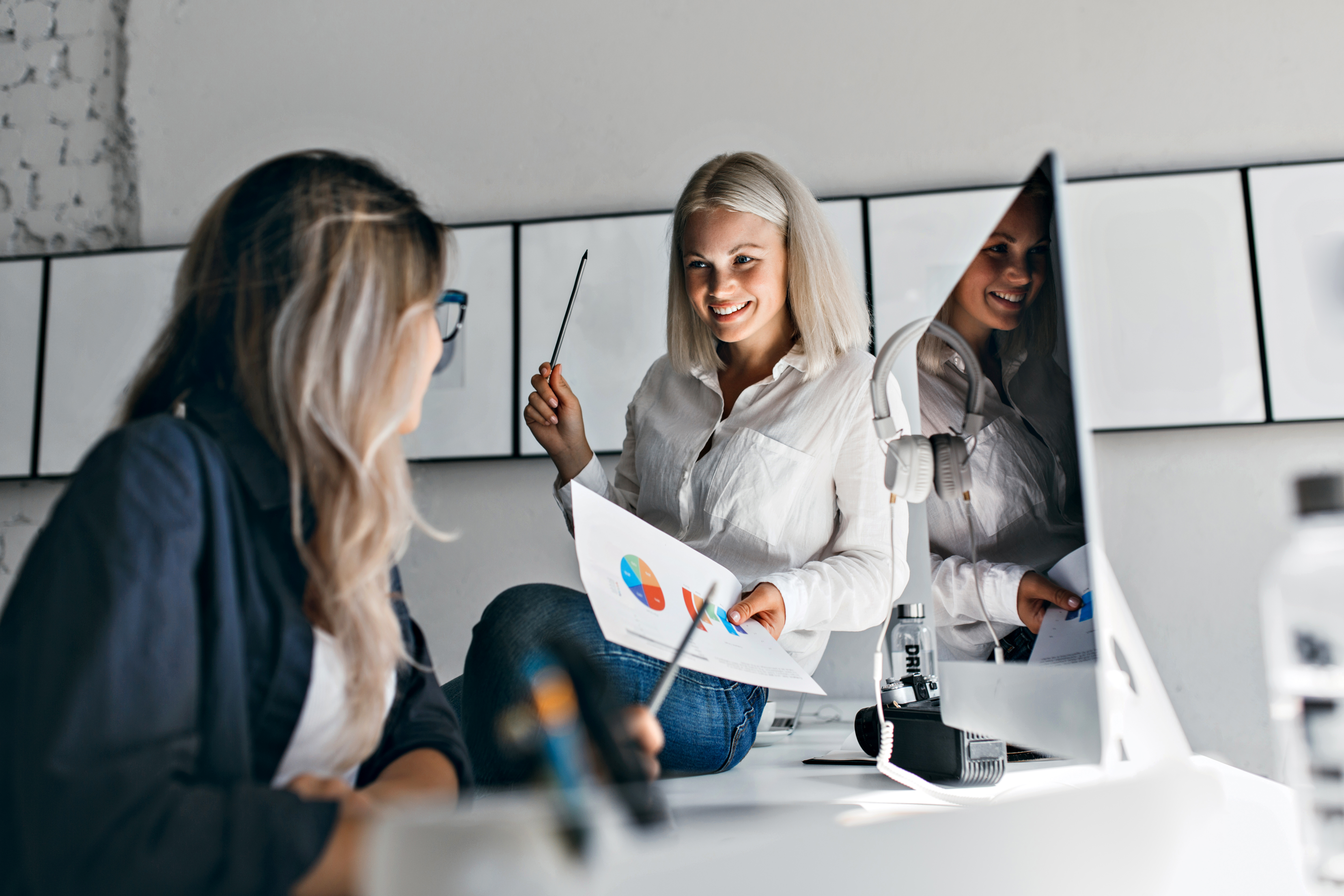 smiling-blonde-female-manager-holding-infographic-pencil-while-sitting-table-indoor-portrait-two-women-working-with-computer-office.jpg