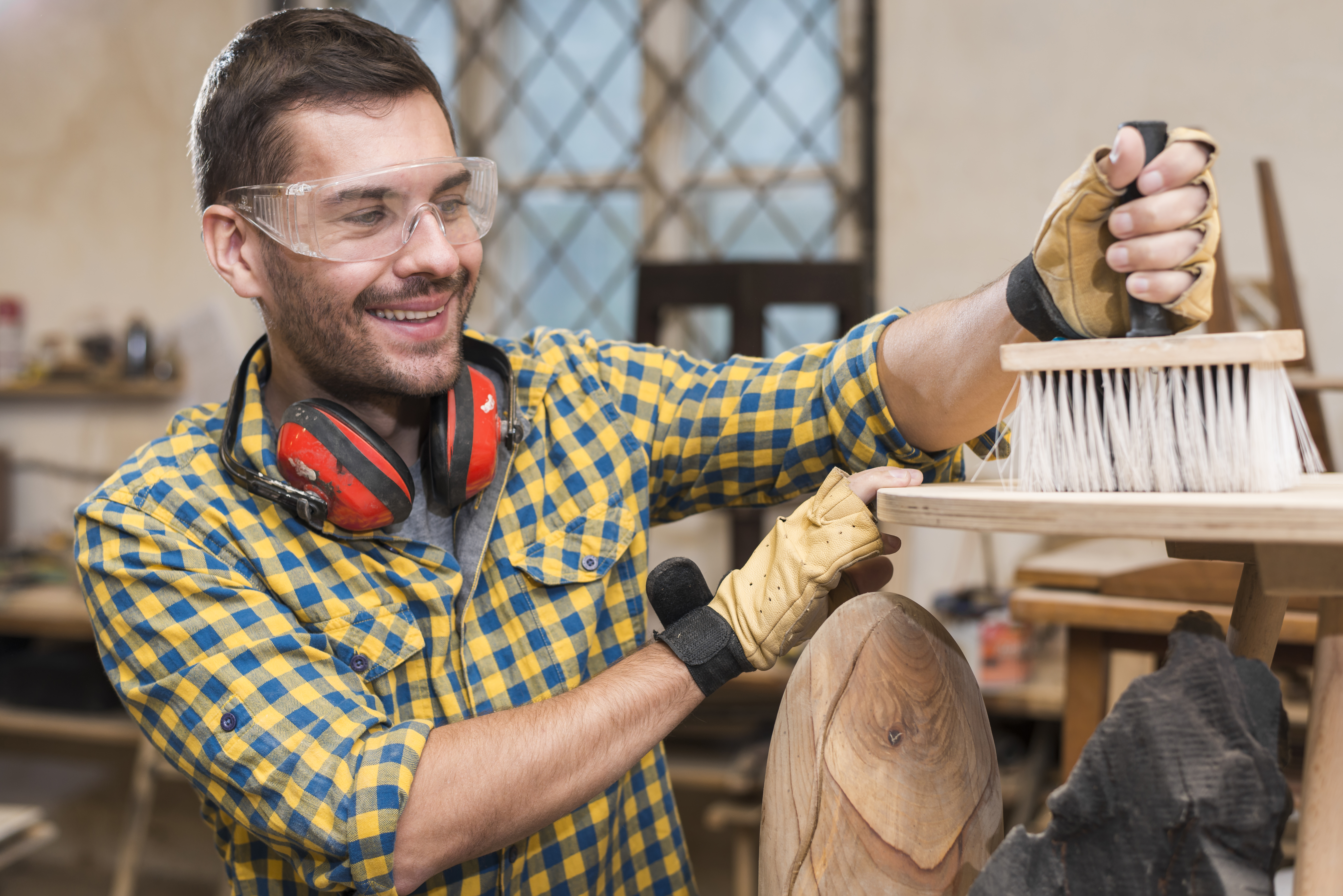 smiling-man-wearing-safety-glasses-ear-defender-around-his-neck-cleaning-wooden-plank-with-brush.jpg