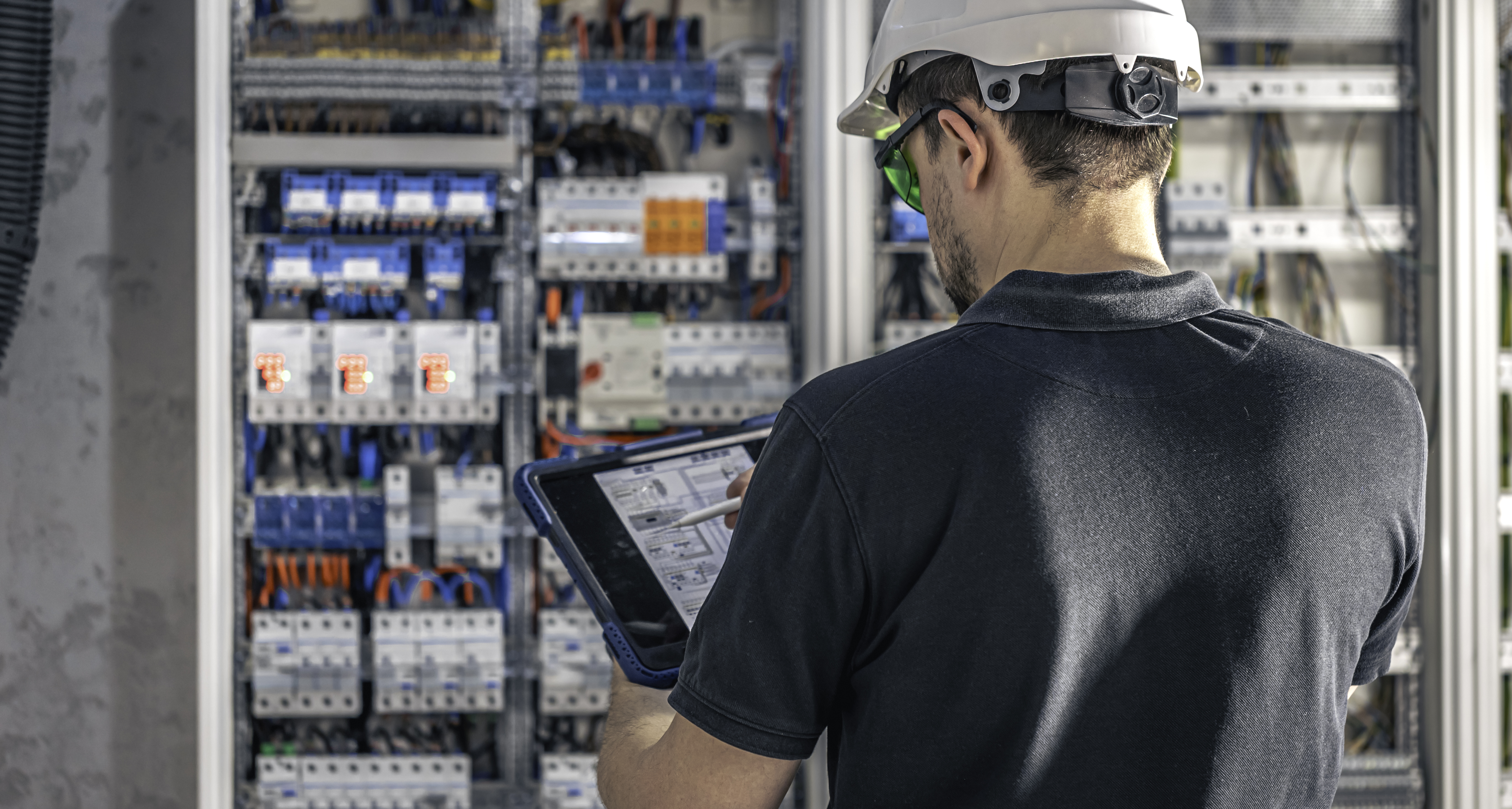man-electrical-working-switchboard-with-fuses-uses-tablet.jpg