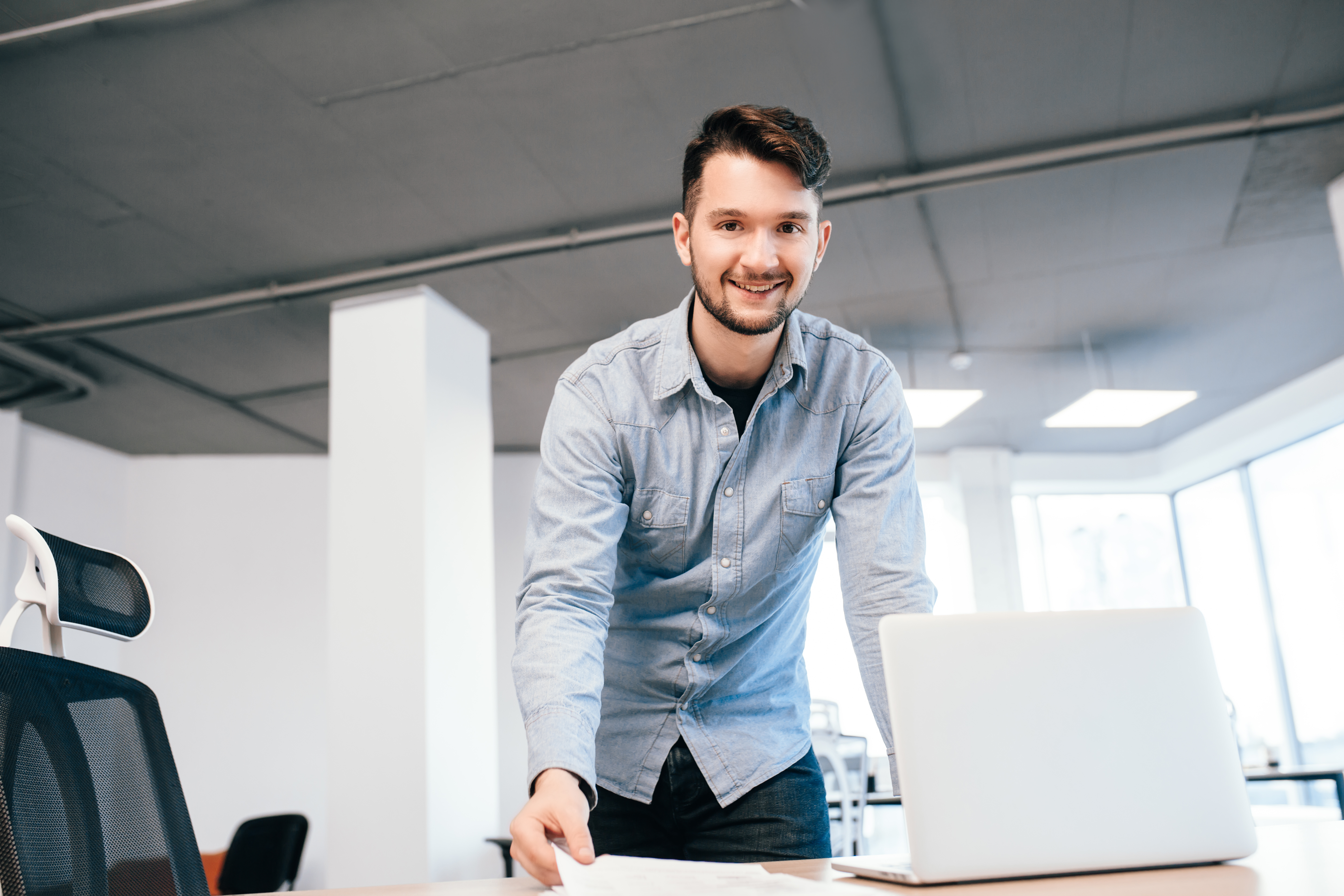 young-dark-haired-man-is-working-with-laptop-office-he-wears-blue-shirt-he-is-smiling-camera.jpg