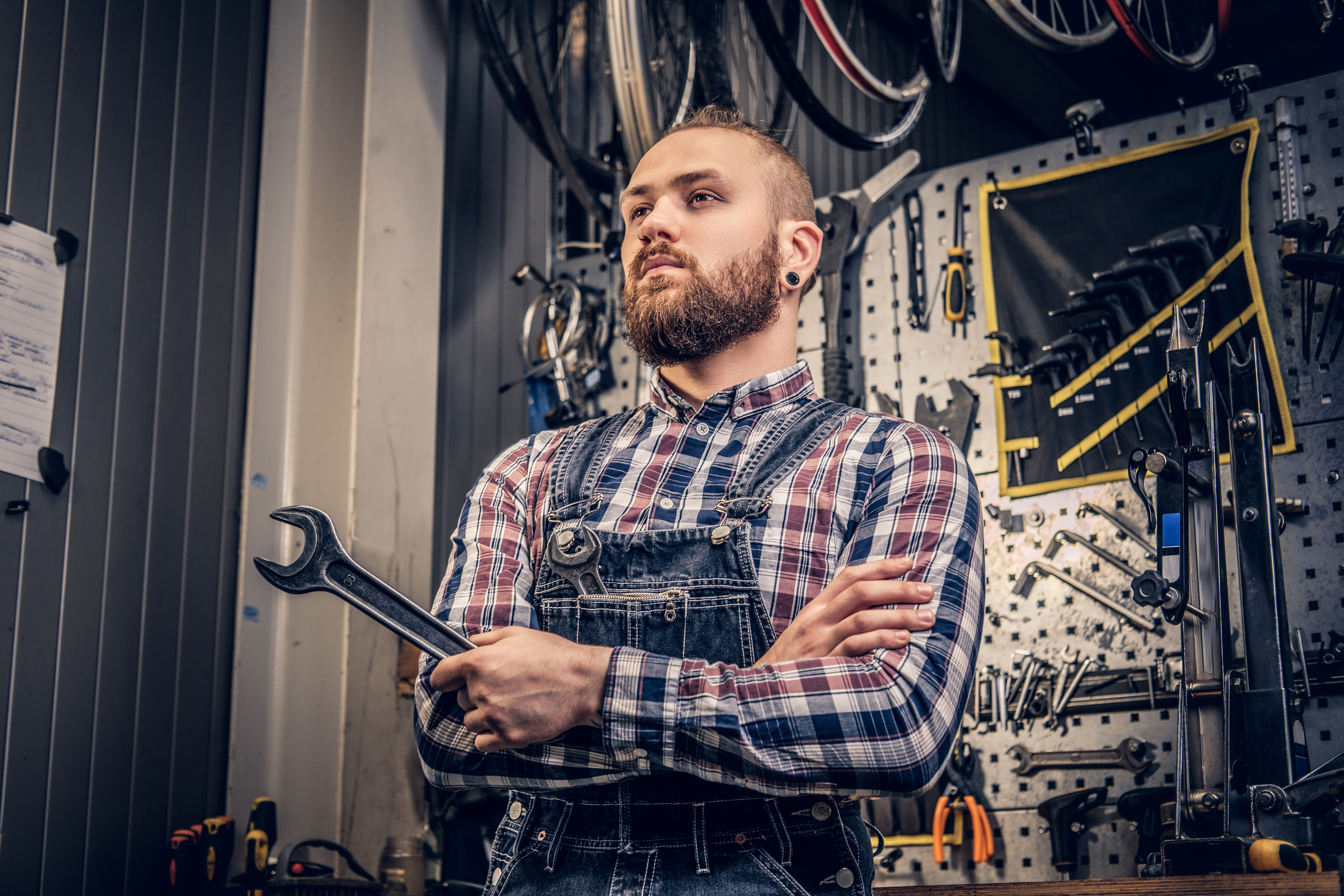 portrait-bearded-bicycle-mechanic-with-crossed-arms-holds-cup-key-tool-stand-background-workshop.jpg