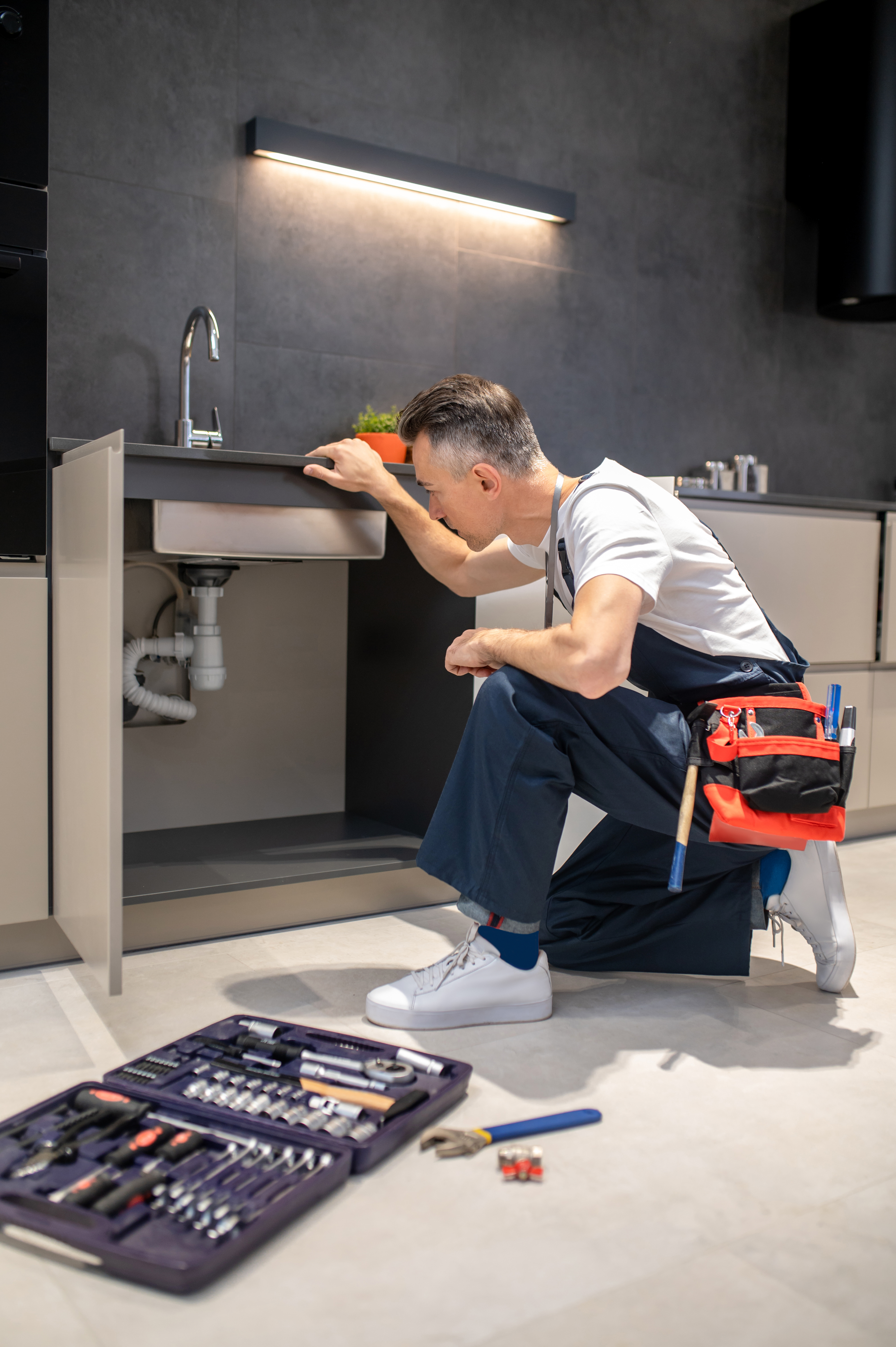 man-kneeling-down-touching-sink-inspecting-pipes.jpg