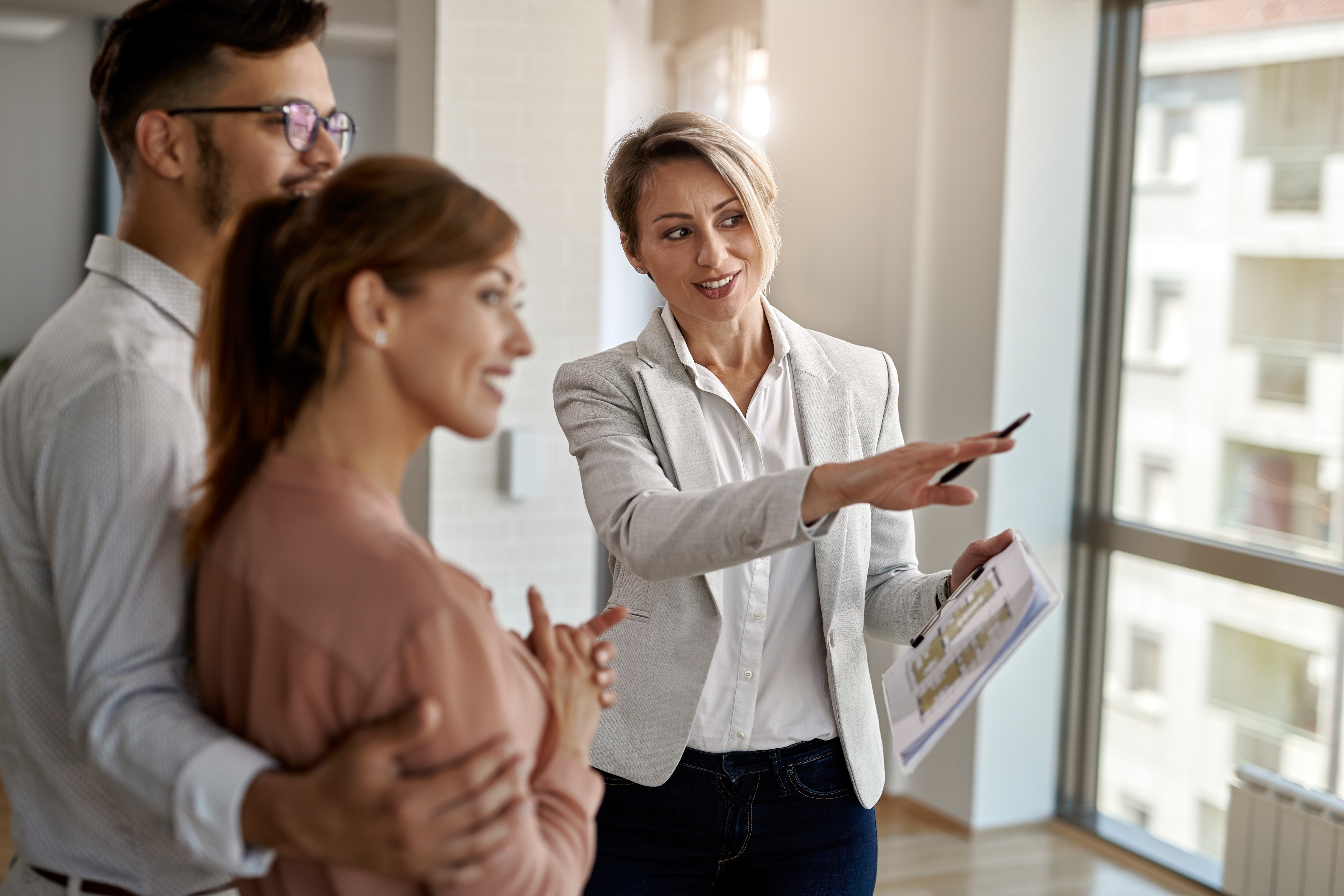 smiling-real-estate-agent-talking-with-couple-interested-buying-new-home.jpg