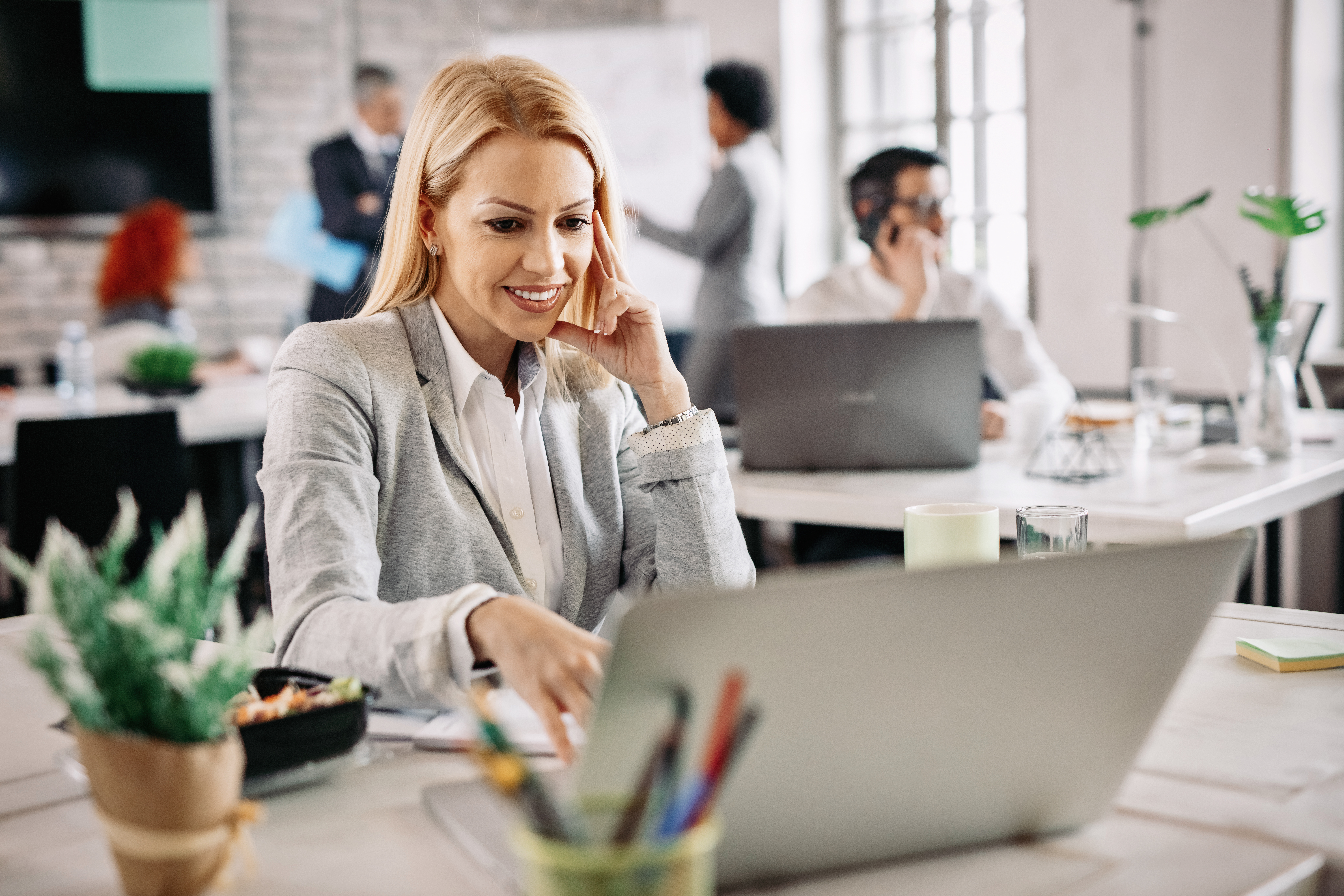 happy-mid-adult-businesswoman-using-computer-surfing-internet-while-working-office-there-are-people-background.jpg