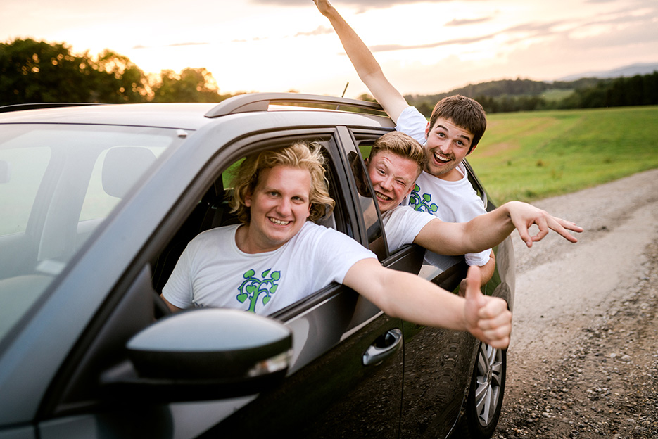 Drei motivierte Fundraiser schauen Grimassen machend aus dem Auto auf dem weg zu ihrem Fundraising Ferienjob