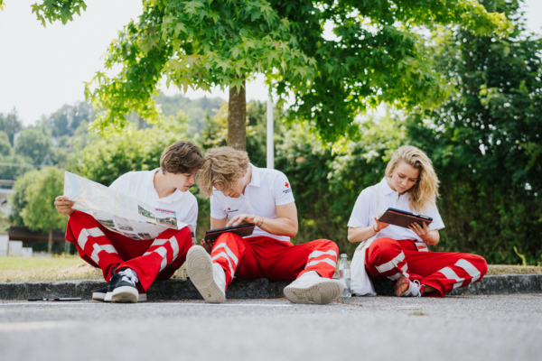 Ein Gruppe Fundraiser sitzt am Boden eines Bordsteigst und schaut auf Tablets, um den Fundraising Tag zu planen