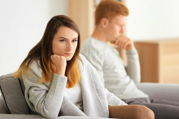 Quarrelled young couple sitting on sofa in light room