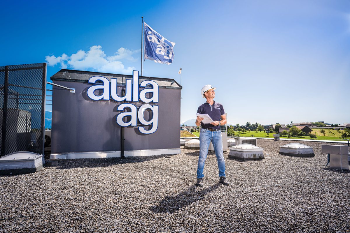 Mitarbeiter der Aula AG auf dem Flachdach vor dem Firmenlogo, Content-Pass