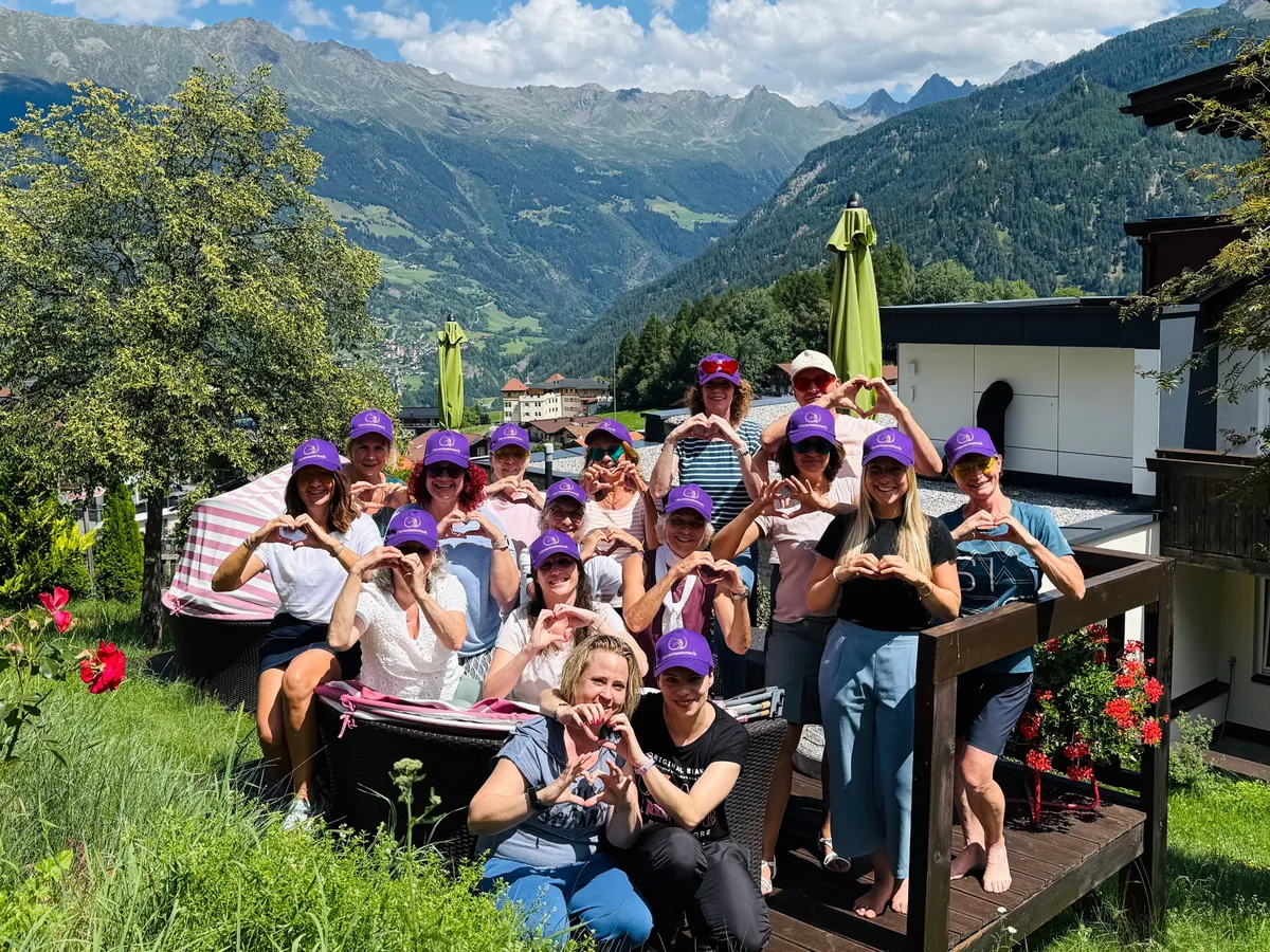 Gruppe beim Retreat in Ladis mit violetten Caps, alle formen ein Herz mit den Händen