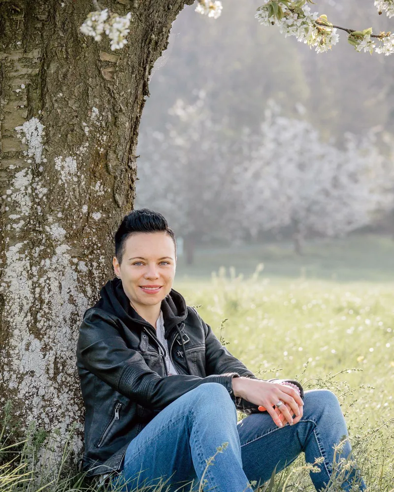 Graziella Wicki sitzt an einen Baum gelehnt in einer Blumenwiese