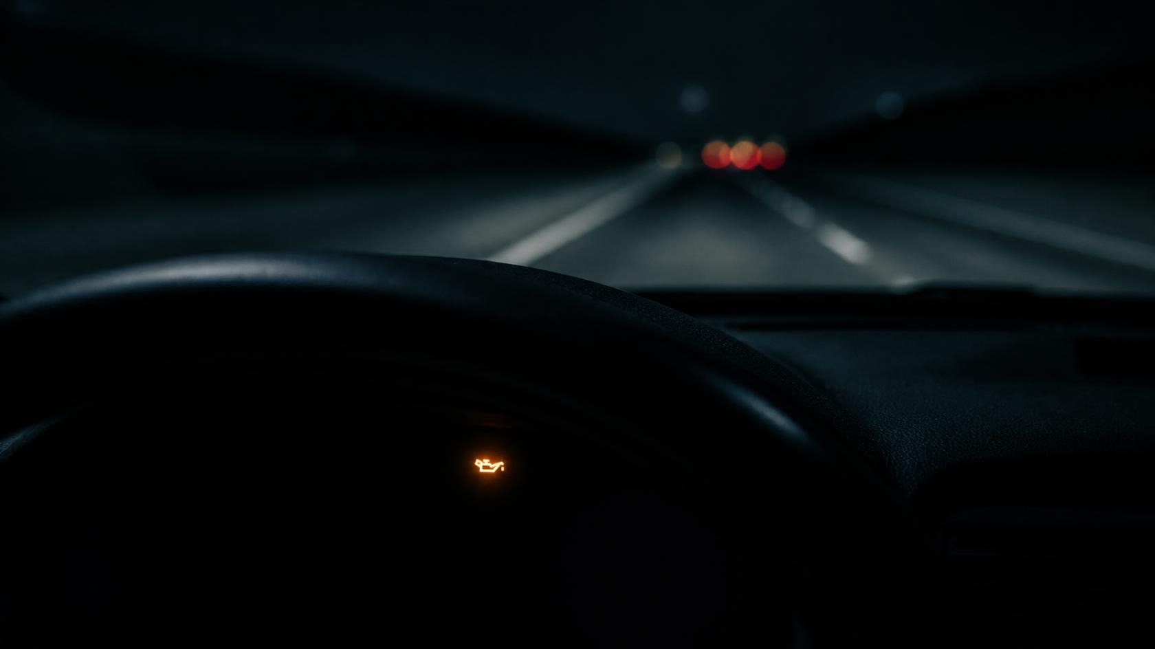 Nächtliche Autobahn aus dem Fahrersitz, eine kleine Öldruck-Warnleuchte glimmt auf dem dunklen Armaturenbrett