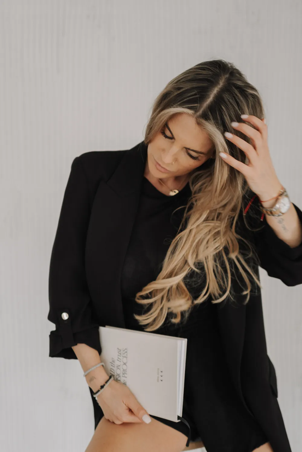 Nina in schwarzem Blazer, eine Hand im Haar, ein Notizbuch auf dem Knie.