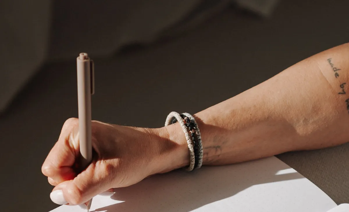 Eine Hand schreibt mit einem Stift in ein aufgeschlagenes Notizbuch.