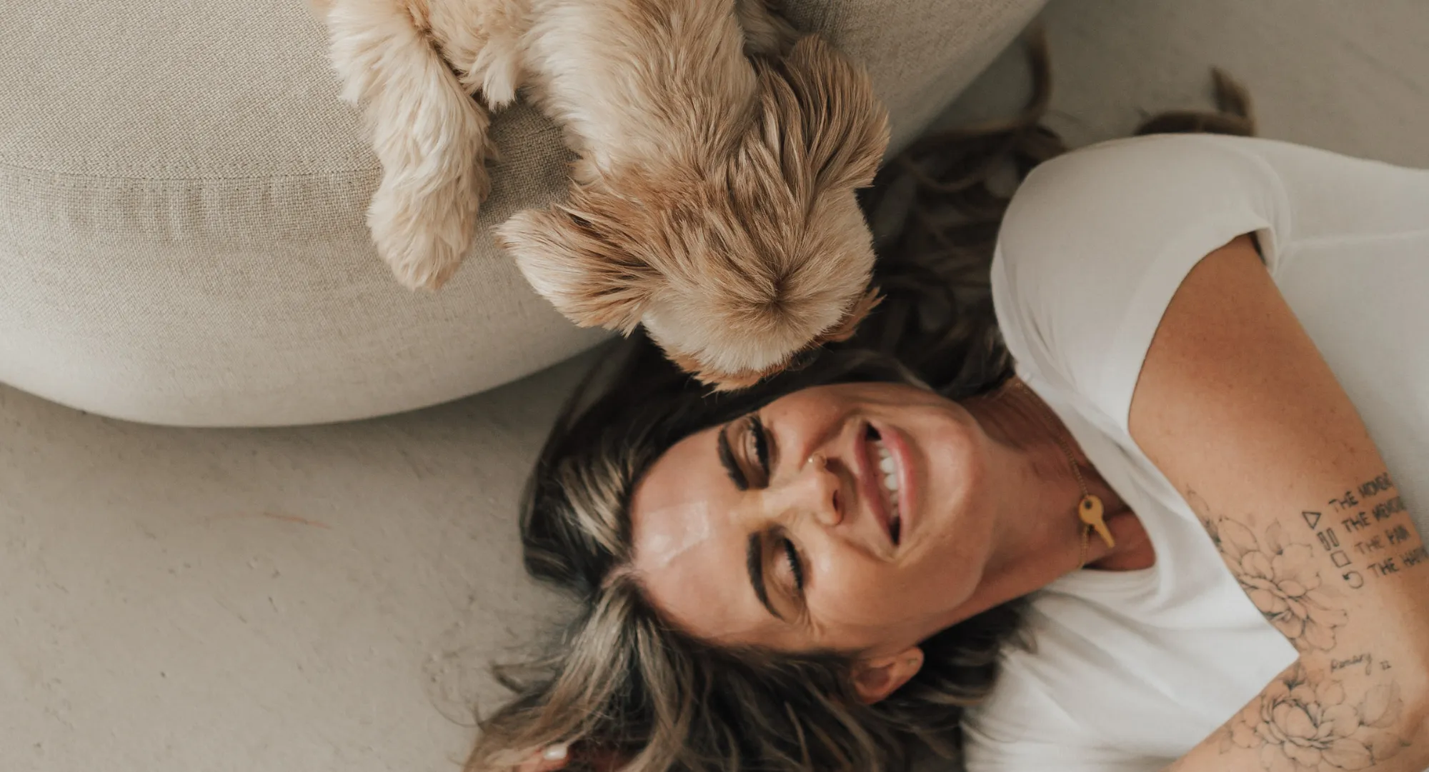 Nina liegt lachend auf dem Boden, ihr Hund stupst sie an der Stirn.