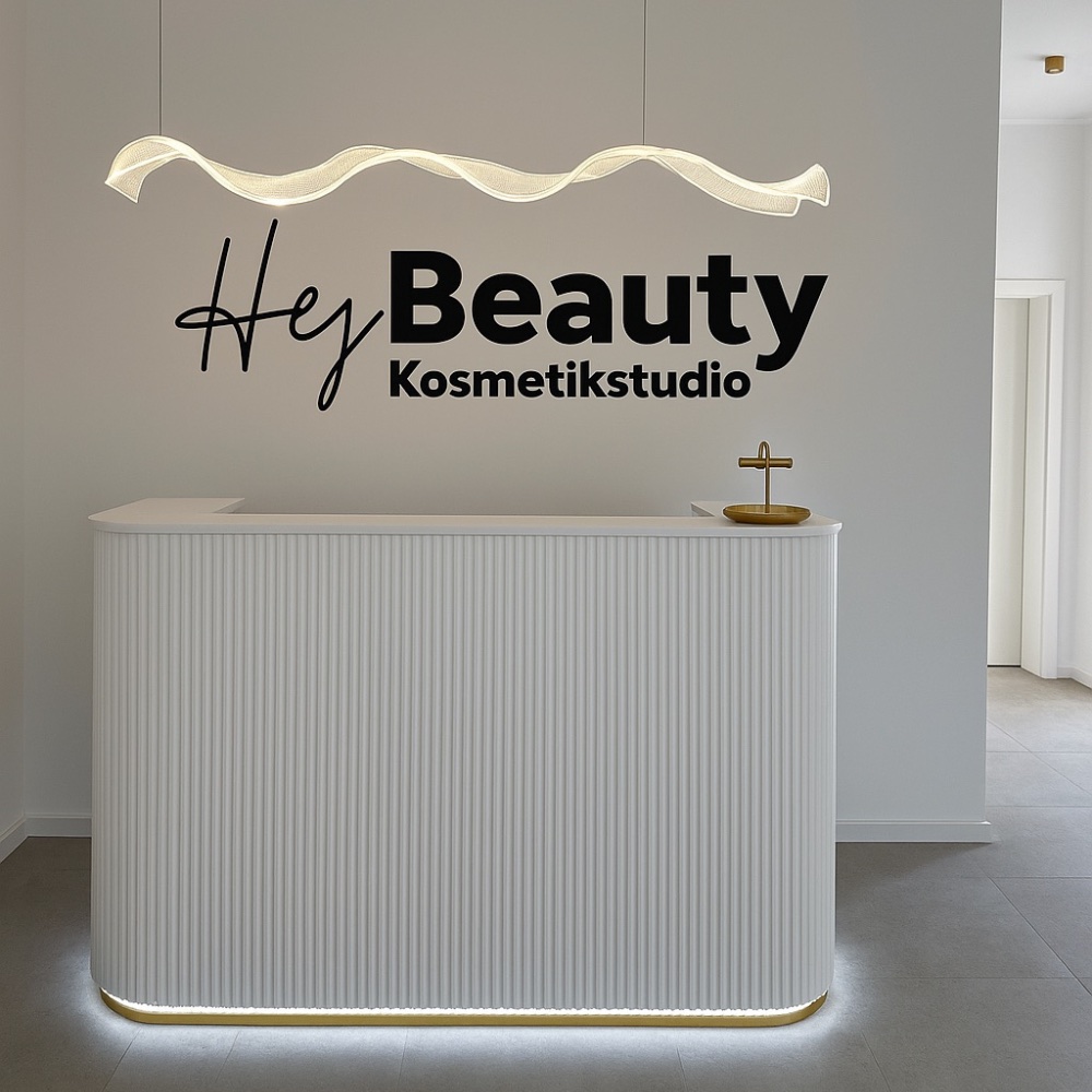 Empfangstheke mit beleuchtetem Logo von HeyBeauty Kosmetikstudio – minimalistisches Design in Weiß und Gold