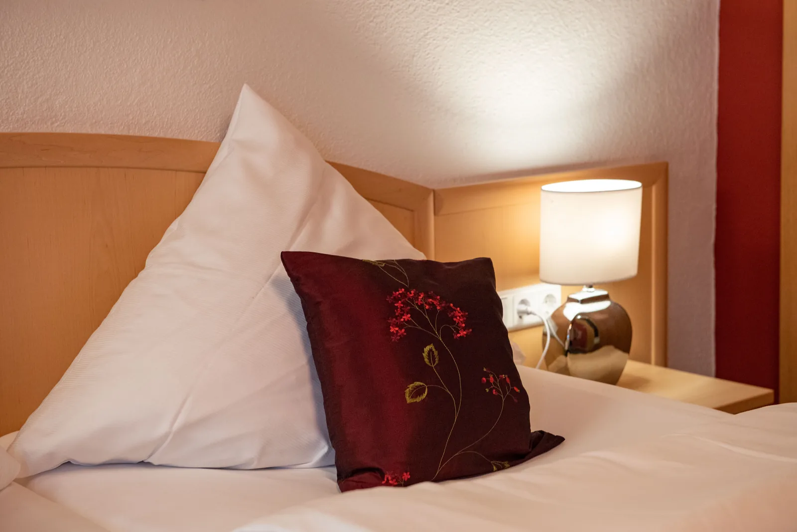 Weiße Bettwäsche und violettes Zierkissen im Gasthofzimmer