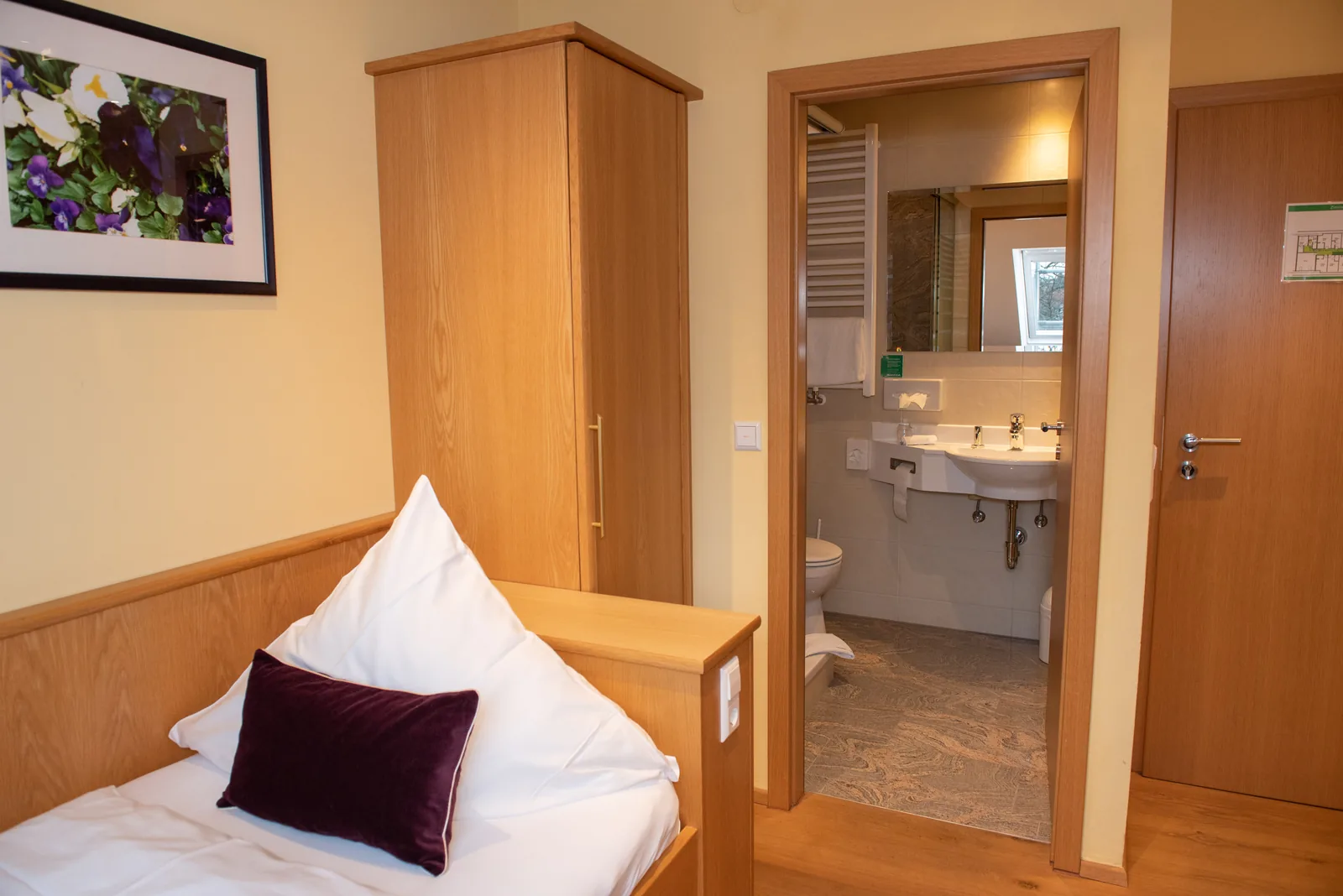 Einzelzimmer mit Bett und offenem Blick zum Bad