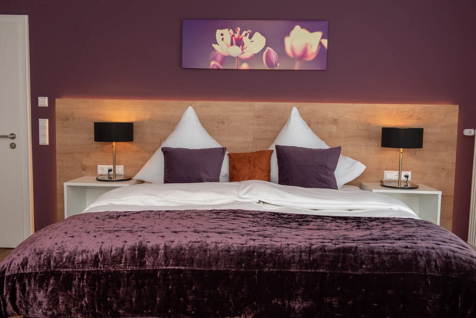 Doppelbett mit violetten Kissen und dunkler Tagesdecke
