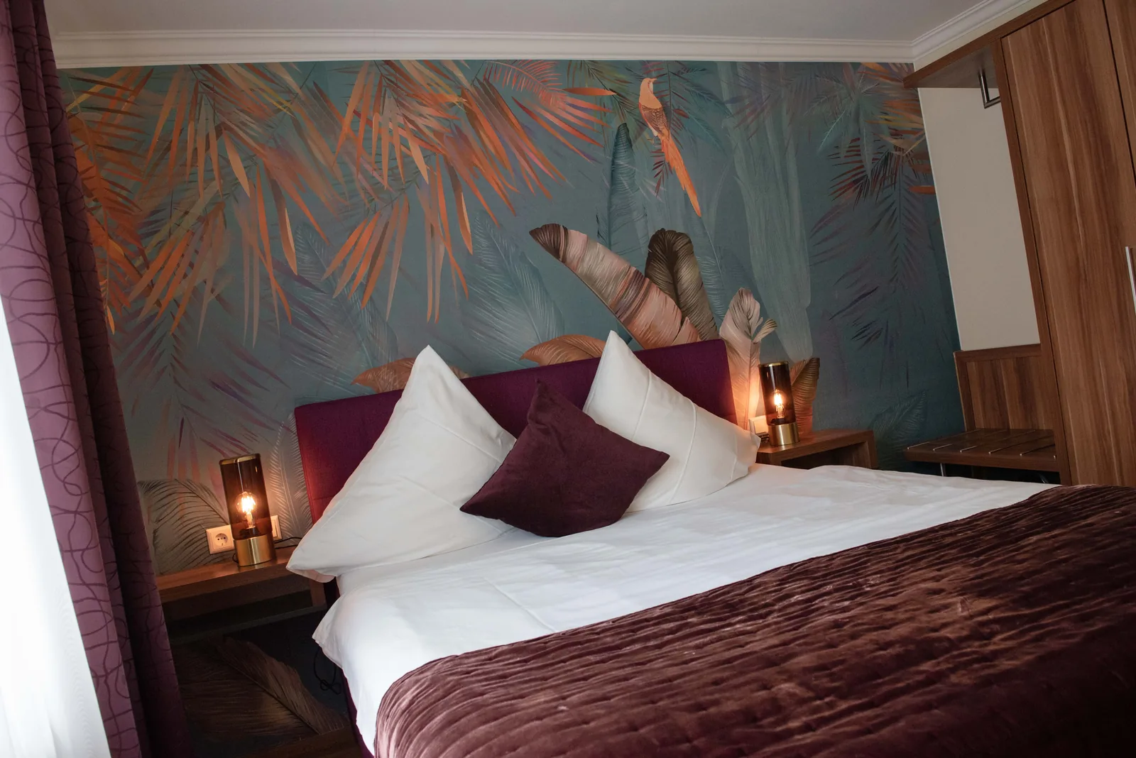 Doppelbett mit violetten Kissen vor Floraltapete