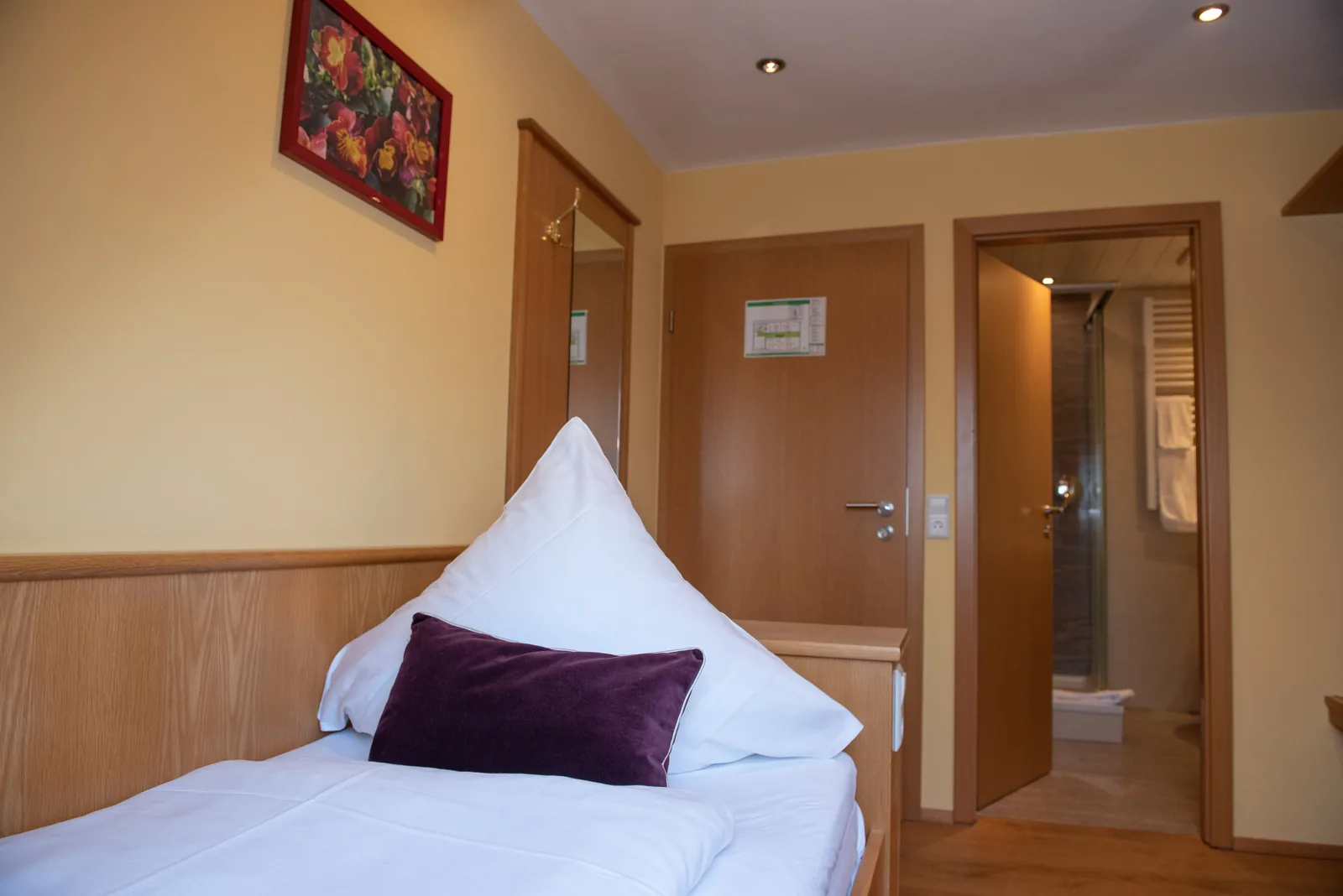 Einzelbett mit violettem Kissen und Blick zum Badezimmer
