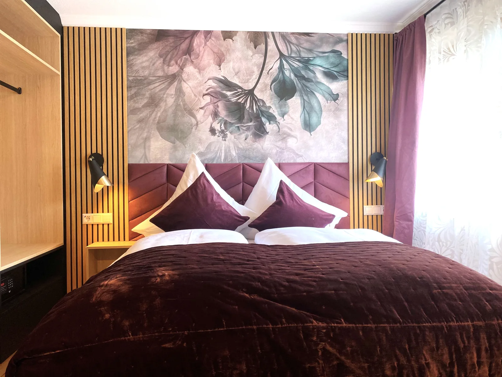 Doppelbett vor Floraltapete und Holzlamellen im Komfortzimmer