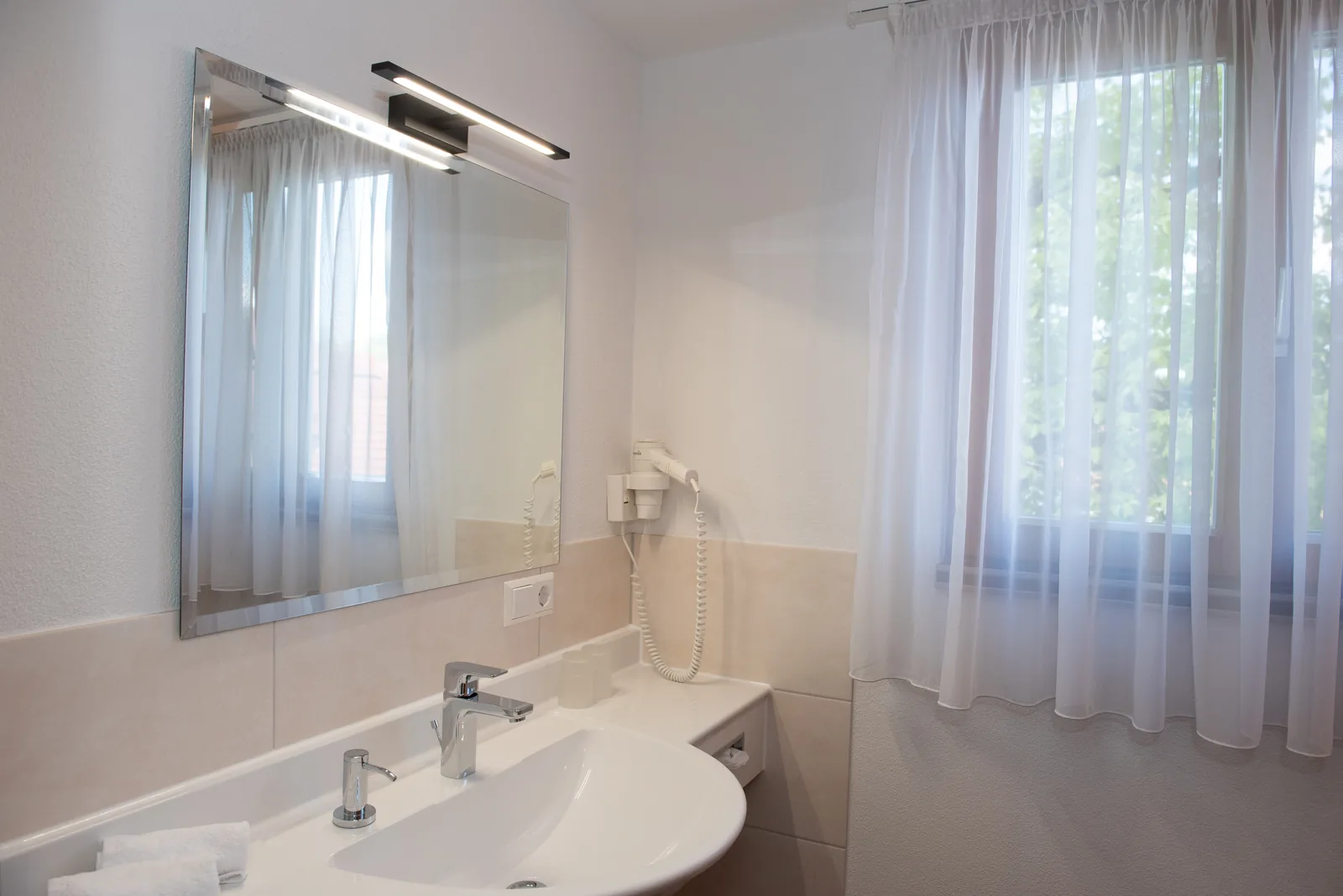 Badezimmer mit Waschbecken, Spiegel und Fenster