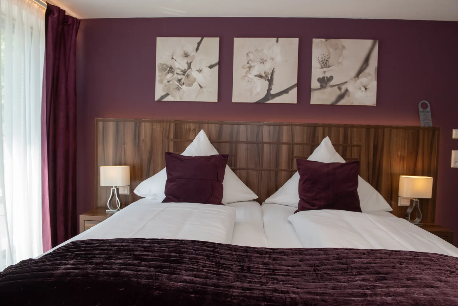 Doppelbett vor violetter Wand mit gerahmten Blumenbildern