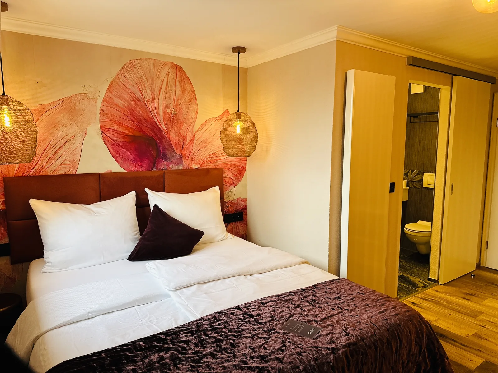 Komfort Doppelzimmer mit farbigem Wandmotiv und offenem Blick zum Bad