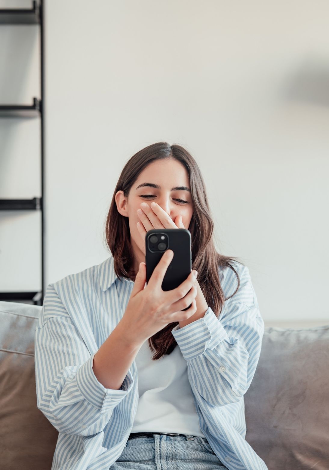 Frau sitzt entspannt auf dem Sofa und schaut lächelnd auf ihr Handy