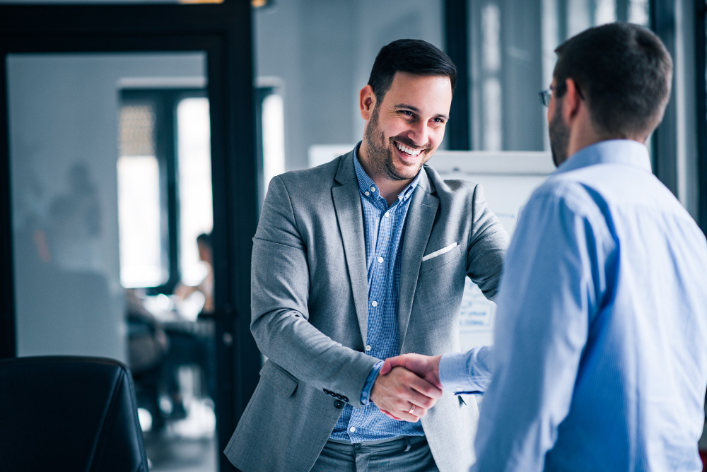 two-smiling-businessmen-shaking-hands-while-standing-office.jpg