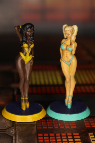 Zwei handbemalte Miniaturen in Bikinis – eine dunkelhäutige Figur in Gelb, eine blonde Figur in Türkis, ideal für Szenen mit Strand- oder Freizeitthema.