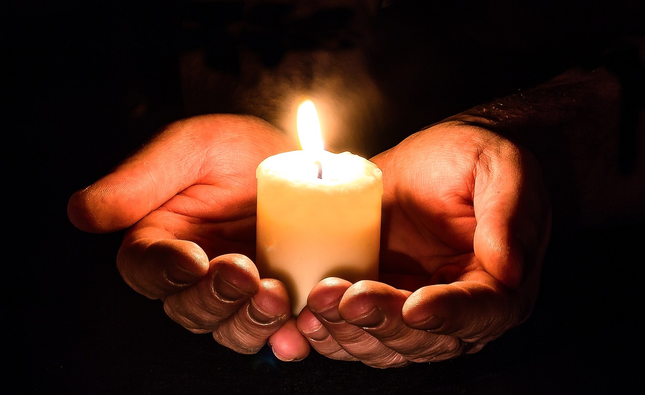 Zwei geöffnete Hände tragen eine brennende Kerze.