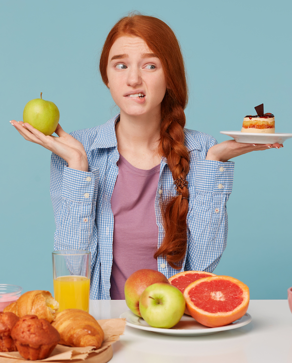 Junge Frau mit gesunden und ungesunden Lebensmitteln macht Diät