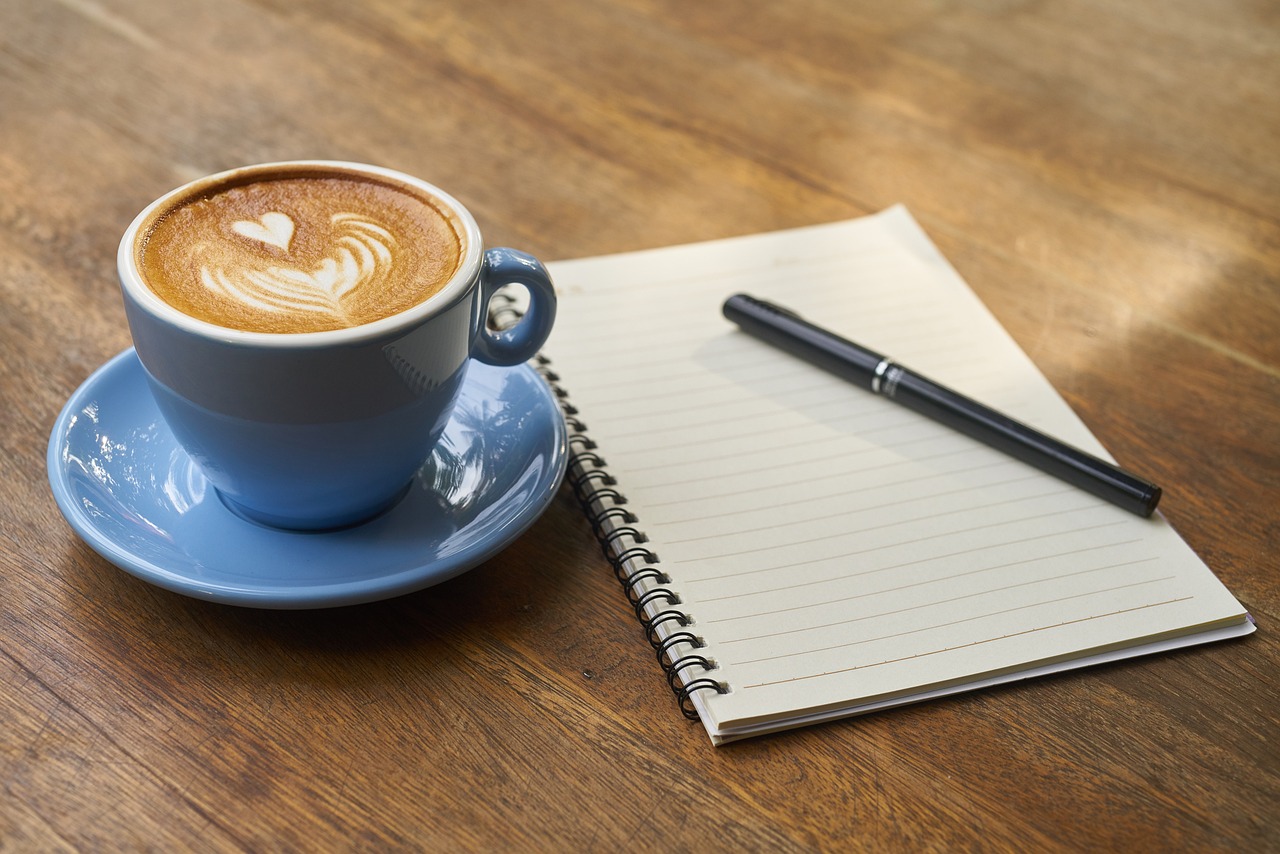Notizbuch mit Stift und Cappuccino auf Holztisch – Symbol für Reflexion, Struktur und persönliche psychologische Begleitung