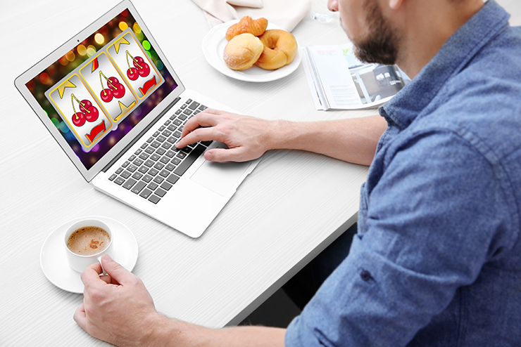 mann mit kaffee spielt online casino slots an laptop