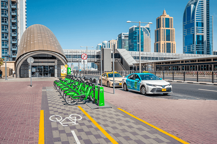 Dubai Straßen und Fahrradweg auf dem leihfahrräder stehen und ein taxi ist im hintergrund vor der dubai skyline zu sehen