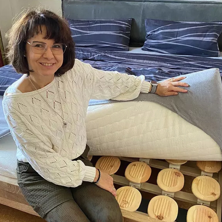 Frau sitzt am Bettrand und hebt Matratze an.jpg